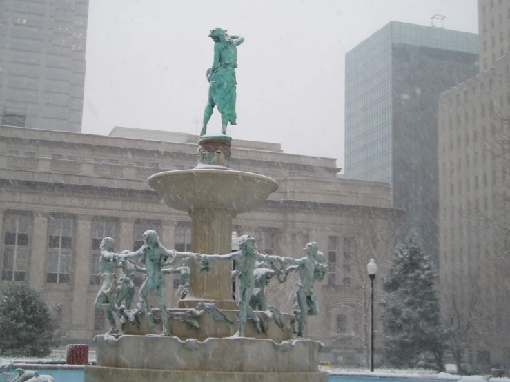 snow falling on a city street and a statue