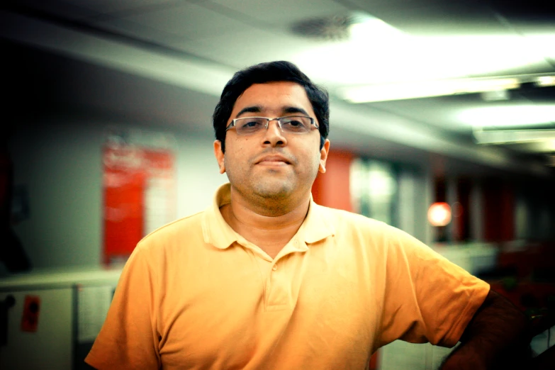 a man in glasses standing up with his arms behind his back