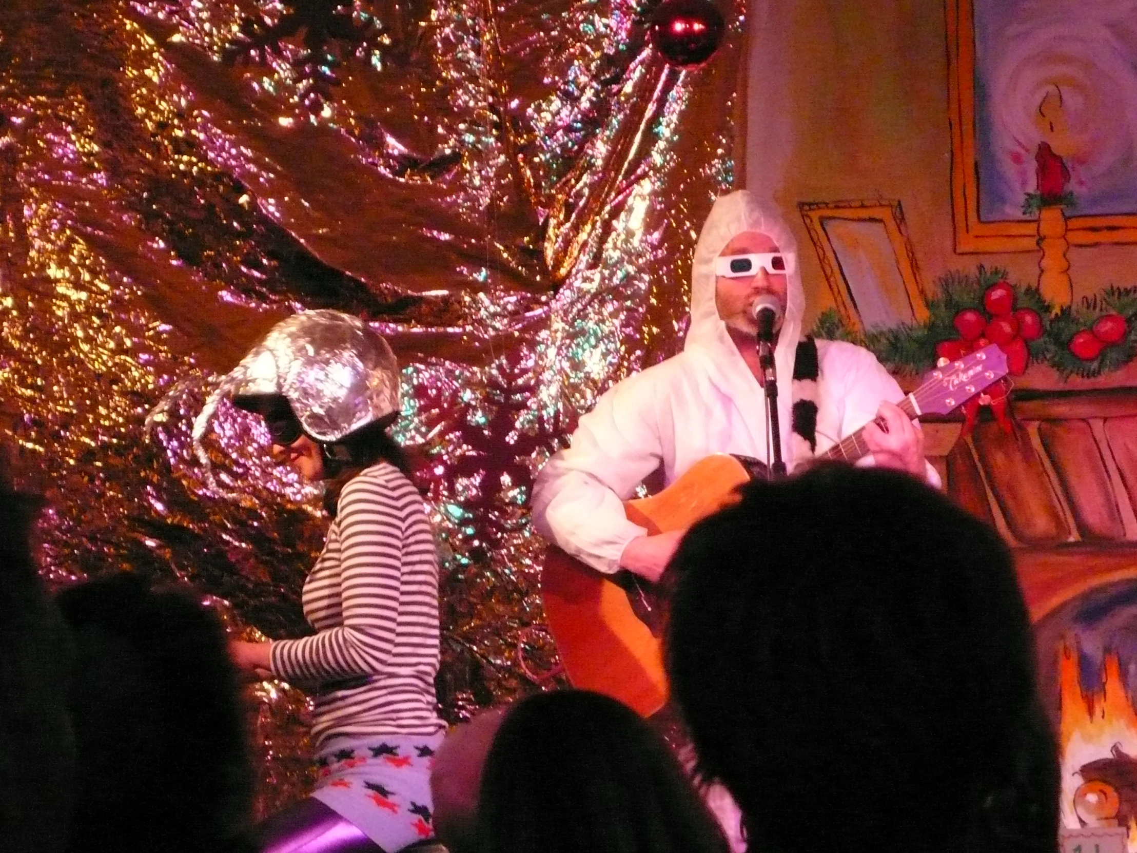 two people with headgear on, playing guitars, singing to a group of people