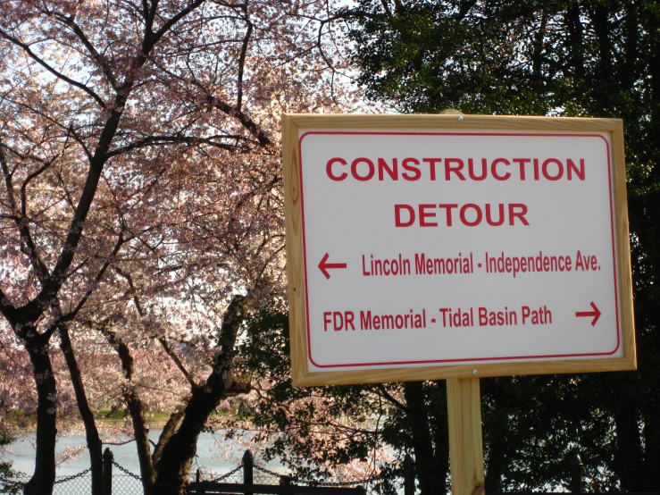 a sign in front of trees and water with a construction detour sign on it