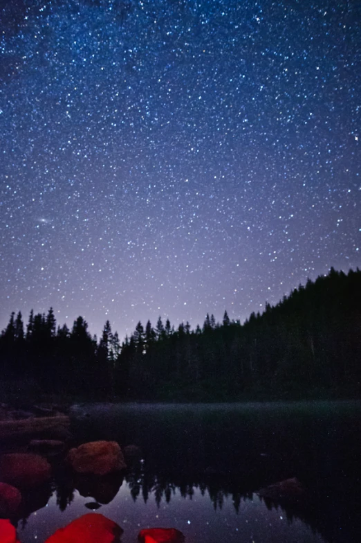 the night sky above a small mountain lake with stars and light shining down