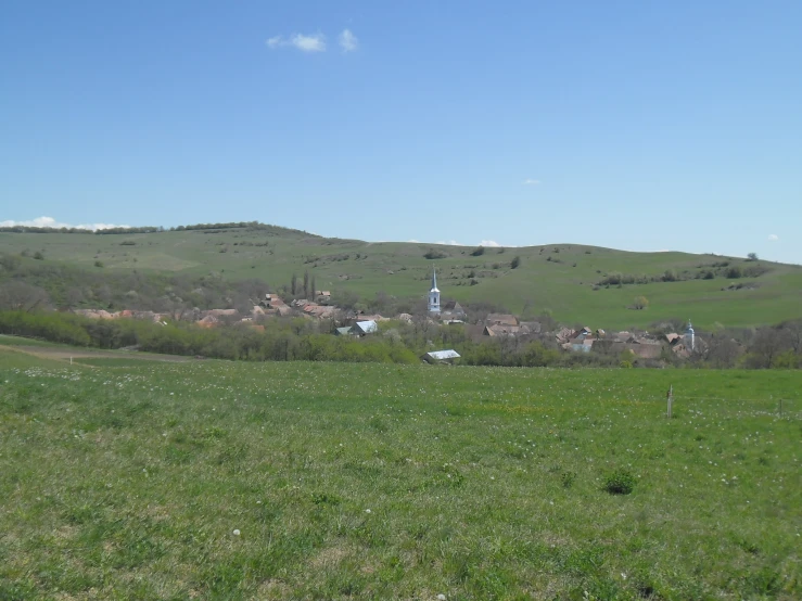 green hillside and houses in the distance with blue sky