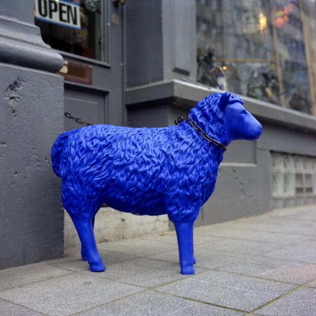 a bright blue statue of a dog stands on a sidewalk
