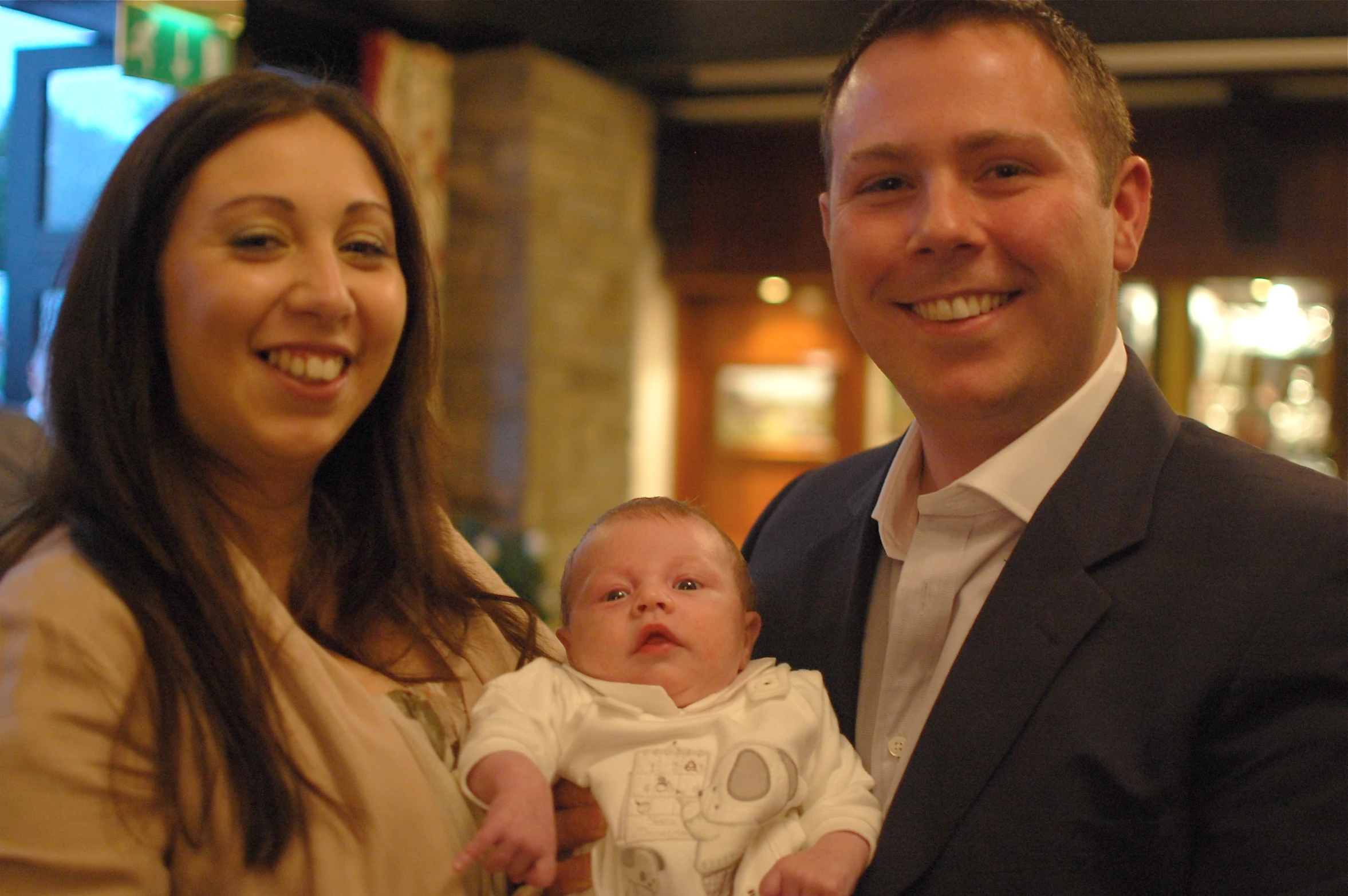 two people smile at the camera while the baby lays on its lap