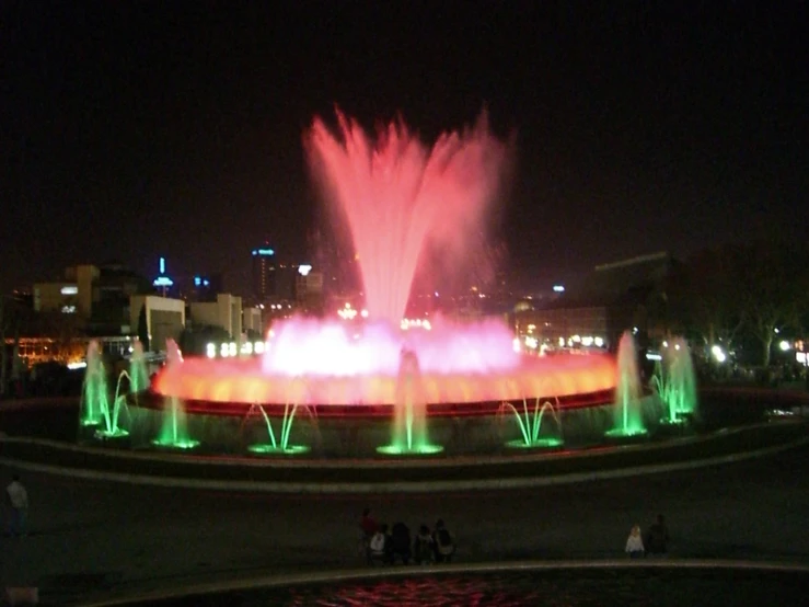 a large fountain with neon lights surrounded by people