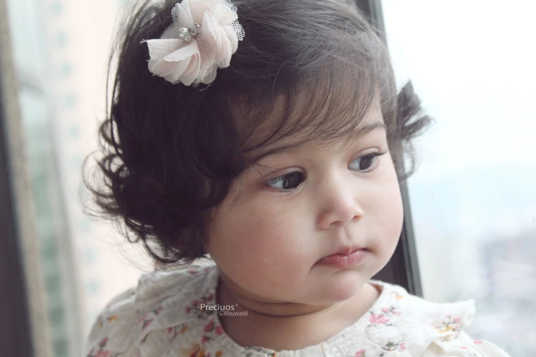 a baby girl with a hair clip in her hair looking out the window