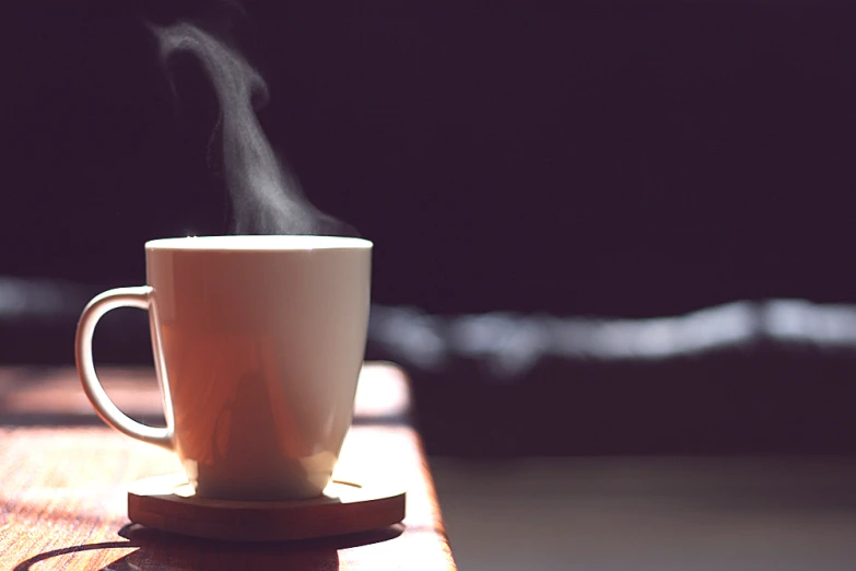 a steaming cup on the table with a wood coaster