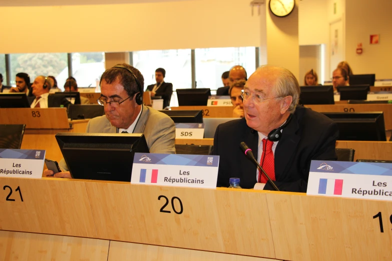 three men sitting behind a podium in front of a number of people