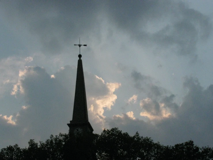 an old church steeple is silhouetted against a cloudy sky