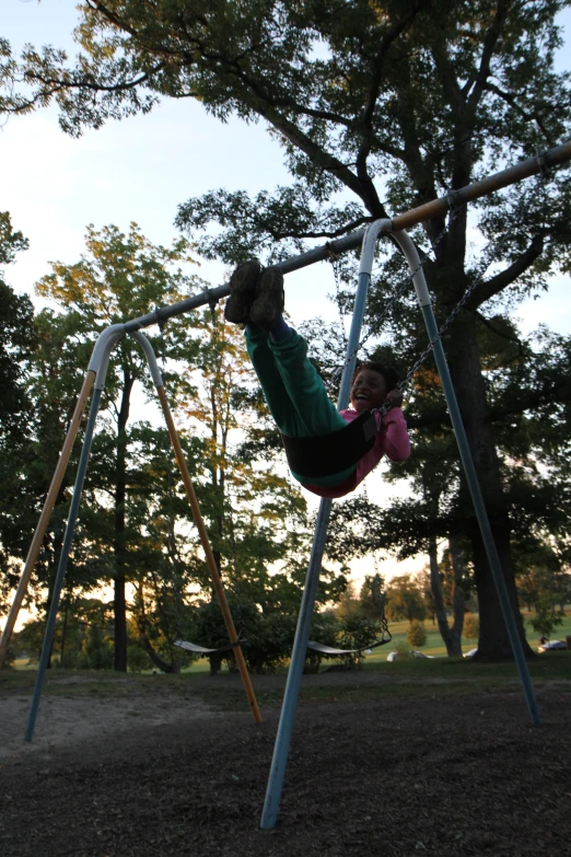 a girl on a swing swinging the bar with trees in the background