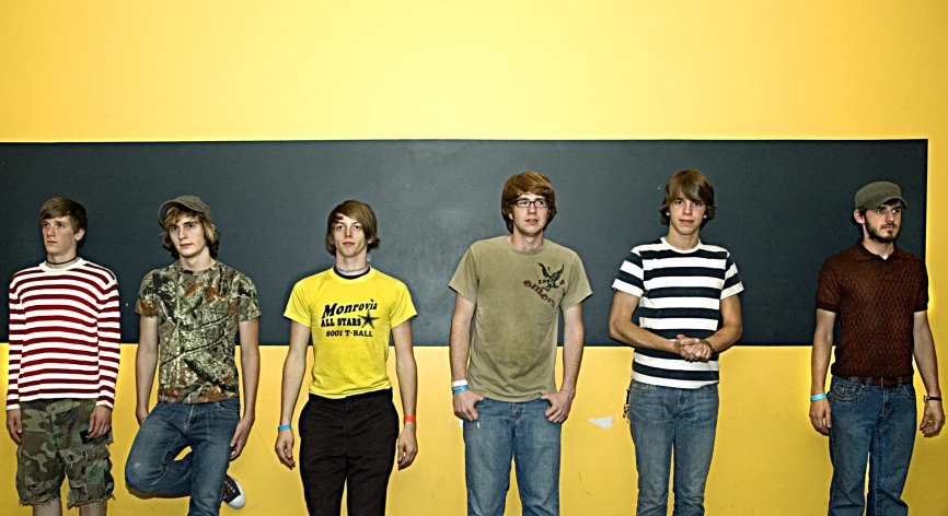 four young men are posing against a black wall
