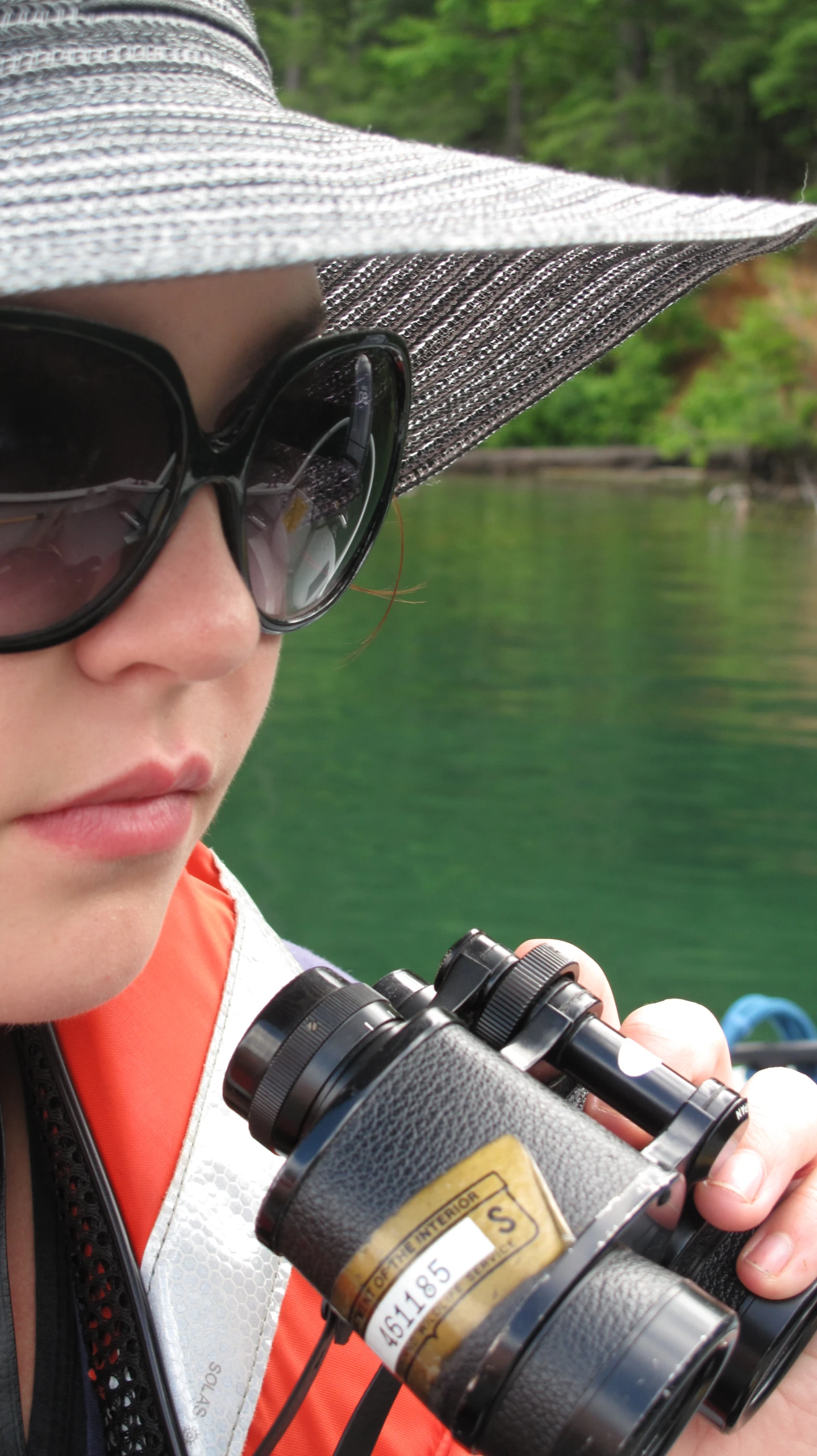 a person wearing sunglasses and a hat standing in front of a body of water with a telescope