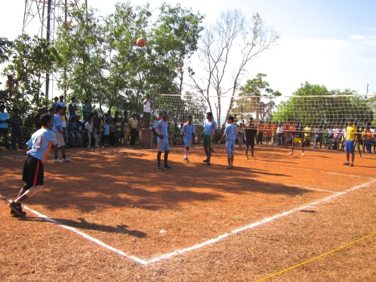 group of young men playing volley ball on dirt field