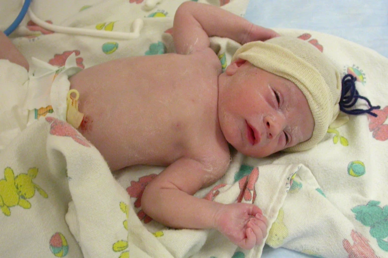 a newborn baby in a white hat sleeping on the blanket