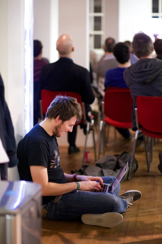 a young man in a black shirt sitting in front of a laptop computer