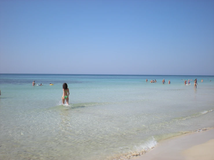 a person stands in the ocean near a beach with clear blue water