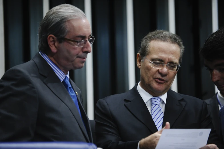 three men in suits standing together and looking at soing