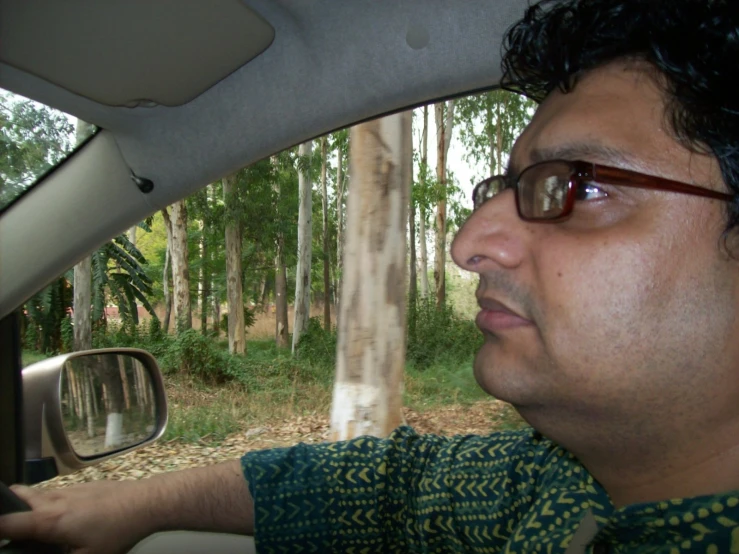 man in glasses sitting in car next to forest