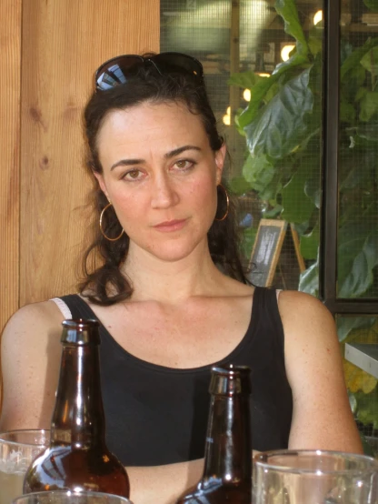 a woman in glasses sitting at a table with two beer bottles