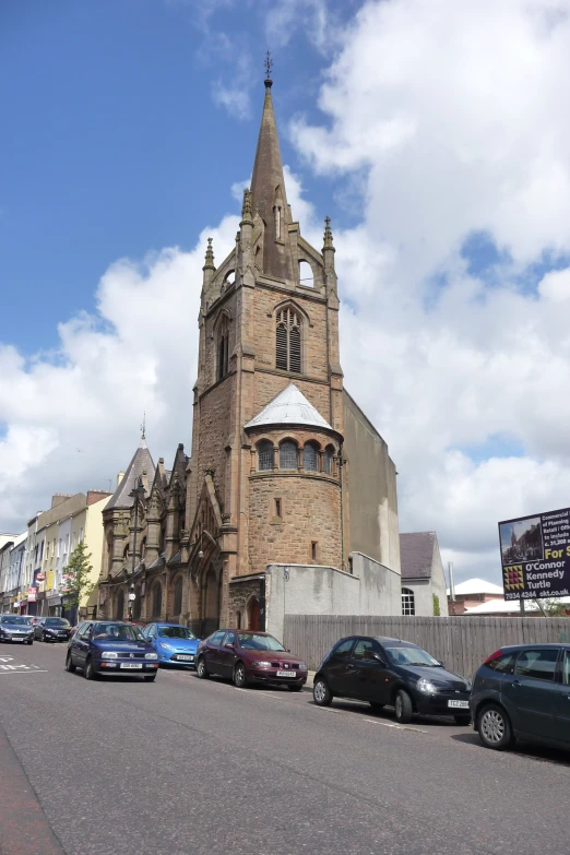 several cars parked in the street below a tall tower with clock