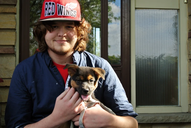 a young man with his hat on holding his small dog