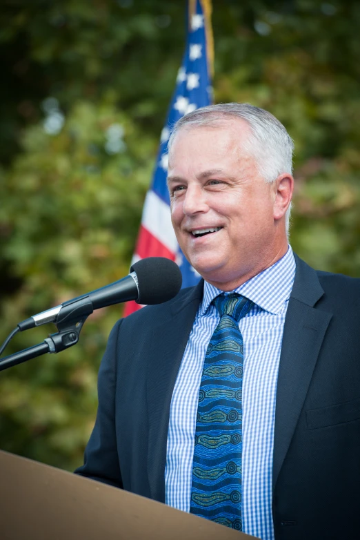 a man stands at a podium and smiles with a microphone in front of him