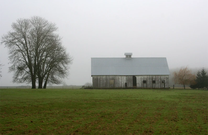 an old barn sits on a foggy day in a country setting