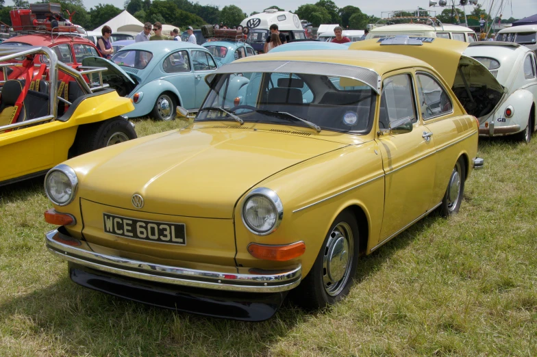 a yellow classic automobile sitting on top of a grass covered field