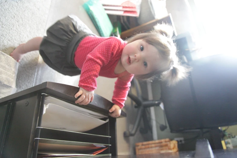 a little girl standing on a microwave and reaching into it