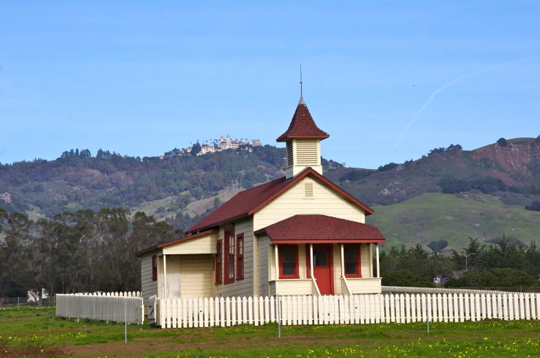 a small church near a white fence and mountains in the background