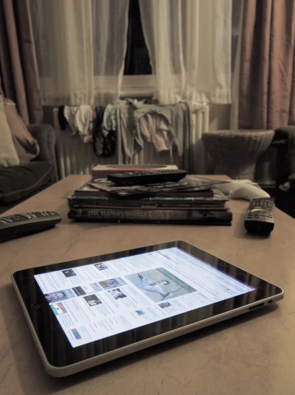 a tablet sitting on top of a table with remotes and papers