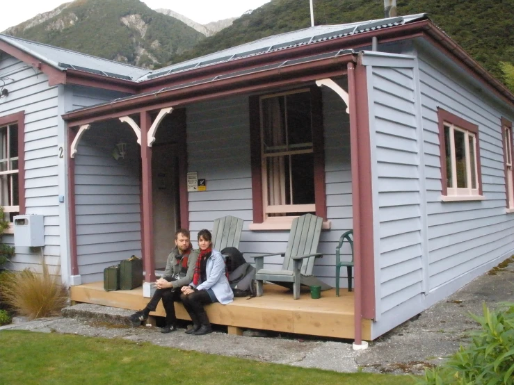 two people sit on a porch outside their home