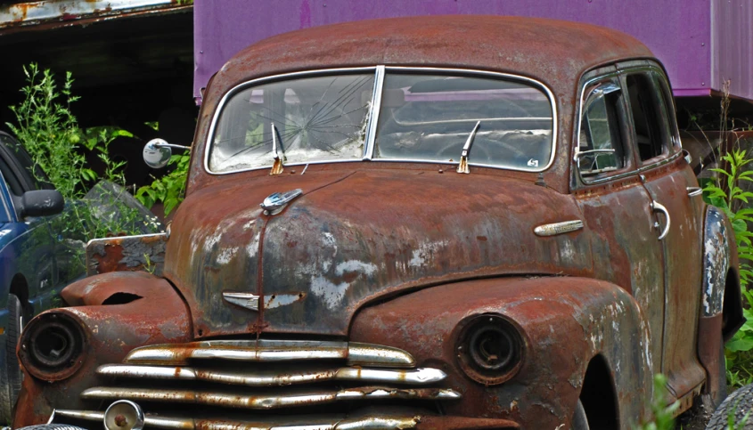 the front of a rusty old car sits abandoned