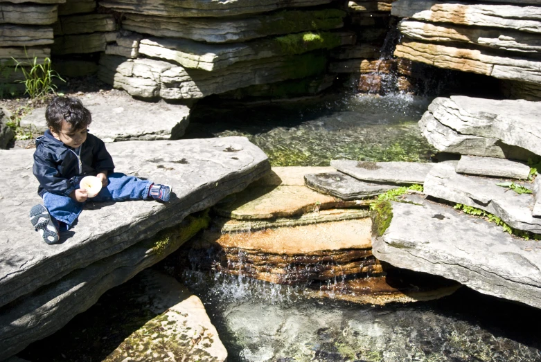 a small child sitting on top of a rock near a river
