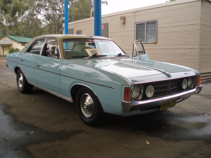 an old blue car parked on a wet parking lot