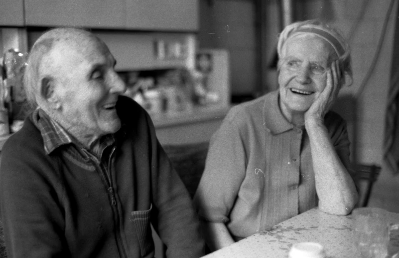 an older woman is smiling while sitting next to a younger man