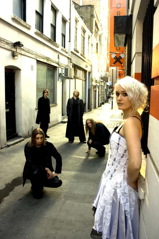 a woman sits against the wall of an alleyway, with another woman in the background