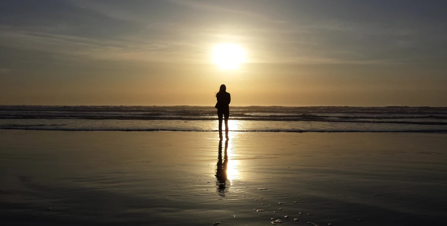 a man stands alone as the sun sets over the ocean