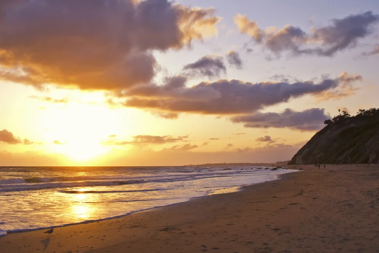 people are standing on the sand near the ocean as the sun goes down