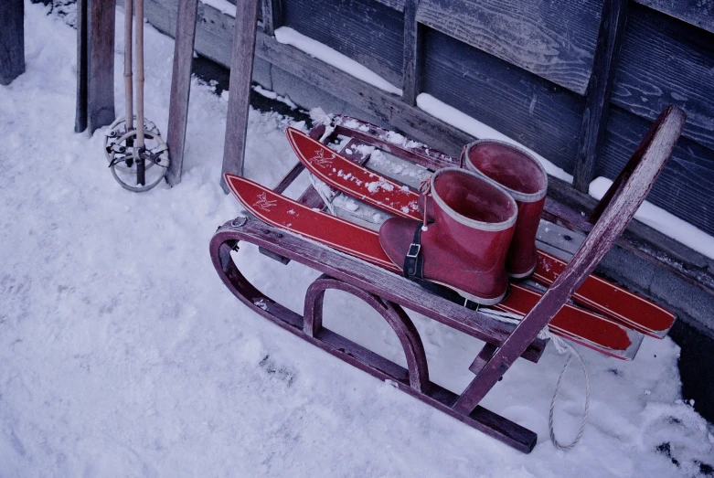 a sled with skis sitting beside it with two snow boots sitting on top