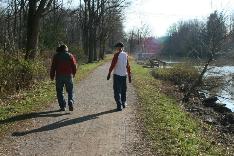 two people walking down a dirt path near a river