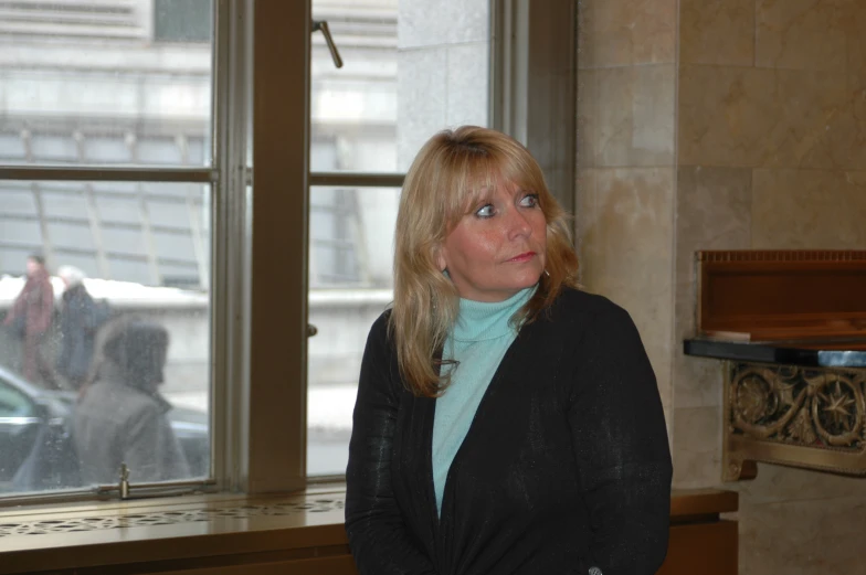 woman in business attire posing with another person looking out a window