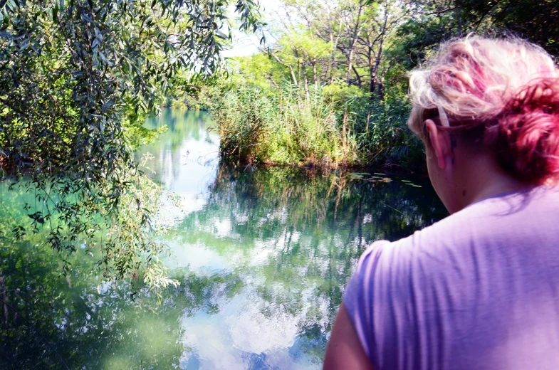woman with id hair looking out on water in the woods