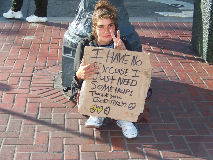 a person sitting on the side walk holding up a sign