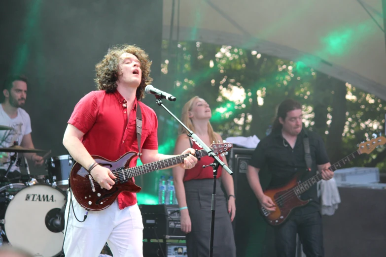 a group of people singing on stage with one guitar player in red shirt