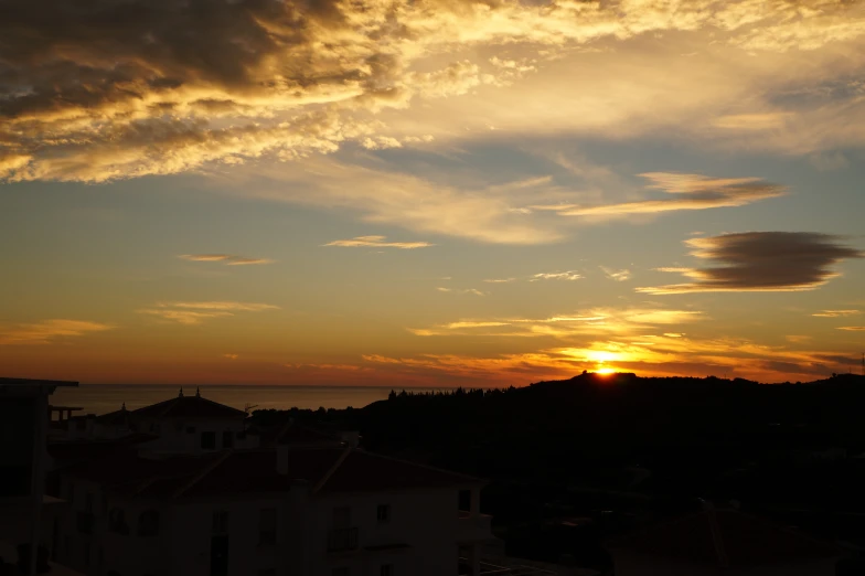 a sunset behind a tower and tree tops over the ocean