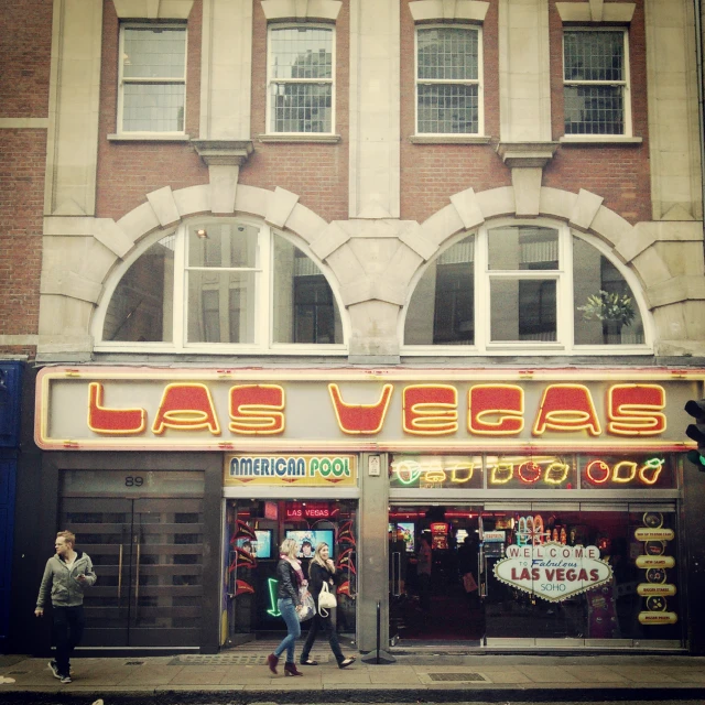 people walking by a las vegas neon sign in front of a brick building