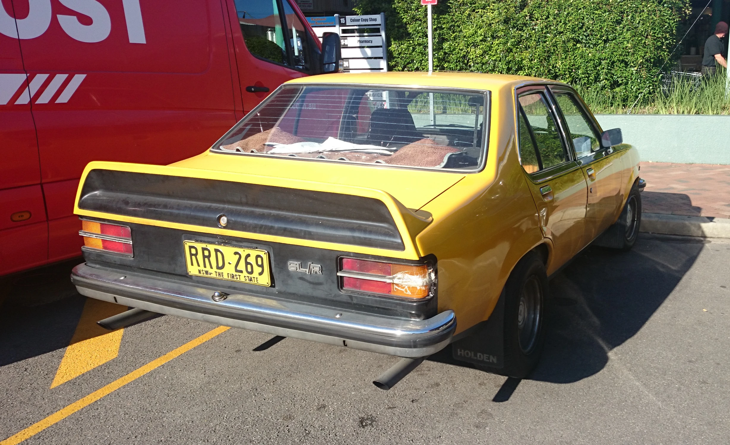 the rear end of an old car with a yellow front door sitting in a parking lot