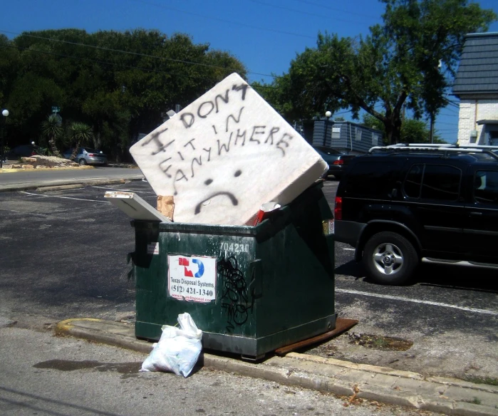 a dumpster sitting on the sidewalk with a sign and trash