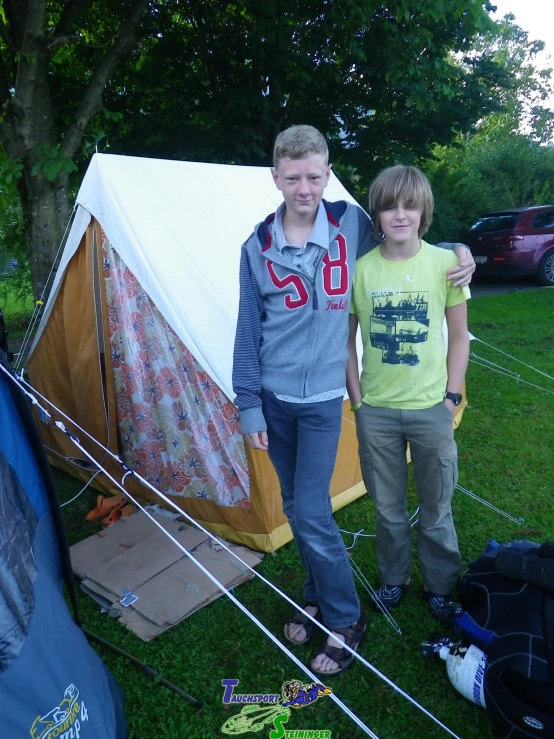 two boys standing next to a tent on the grass